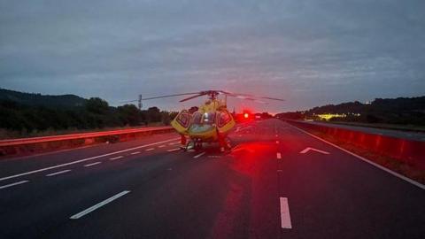 A medical helicopter landed in the middle lane of the M5 motorway. The sky is still dark as dawn hasn't broken yet. 