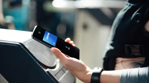 A person paying at a ticket barrier using a phone.