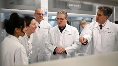 PA Keir Starmer and Ed Miliband wearing white coats talking to staff at the National Nuclear Laboratory facility 