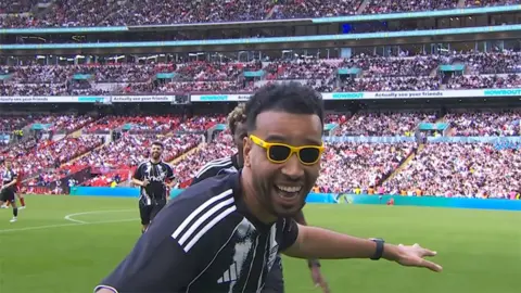 Sidemen YouTube Livestream Niko Omilana from the Sidemen wearing yellow sunglasses as he celebrates a goal.