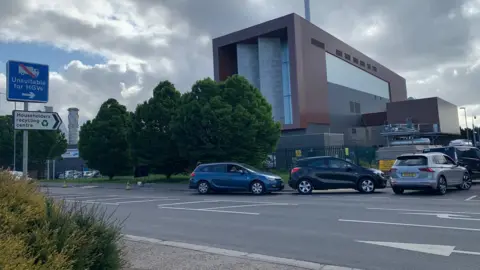 Cars queue to get into the recycling centre, which is a large industrial building.