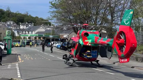BBC Welsh Air Ambulance is parked on a road. Two police officers are walking on the road.