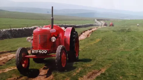 Dave Harrison A small red tractor parked on a countryside track.