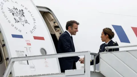 Getty Images French President Emmanuel Macron stepping off plane in Mayotte, greeted by a woman 