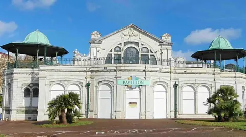 Guy Henderson The Pavilion on Torquay seafront, a building faced with white tiles and topped with a pair of green domes. There is a sign over the door that says Pavilion