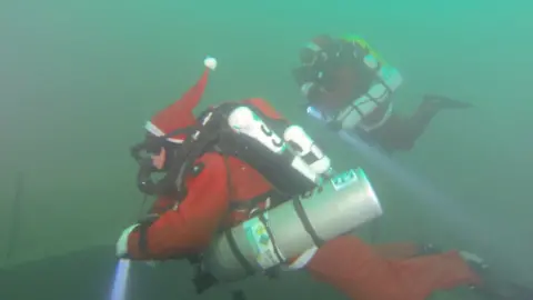 George Birch George in full scuba gear and a Santa costume, including a hat, underwater with a dive partner, also dressed as Santa