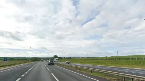Google Street View of the A1 in Lincolnshire. It is a dual carriageway surrounded by green fields with vehicles driving along it 