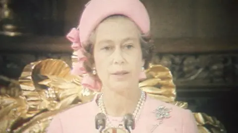 Worn for the Service of Thanksgiving at St Paul’s Cathedral in 1977, this pink ensemble was created by Hardy Amies, adorned with diamond jewellery, with the Queen also wearing the striking pink hat with bow accompaniments by Frederick Fox.