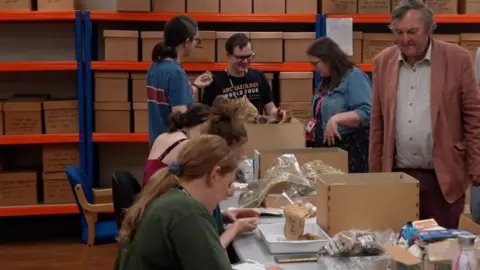 Mark Horton watching volunteers at a table who are unpacking boxes.