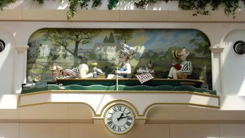 A clock topped with three men rowing a boat surrounded with ducks. 