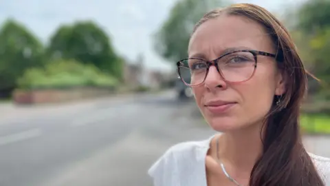 Young woman with a white top and large glasses standing next to a road