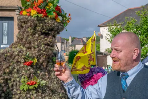 PA Media Burryman being given whisky through a straw