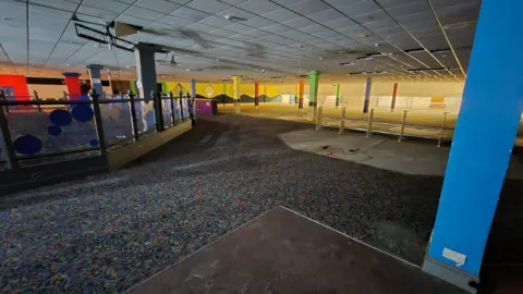 Stuart Woodward/BBC Inside the bowling alley in the Kursaal. It is a large room with white ceiling tiles, blue patterned carpet and blue pillars.