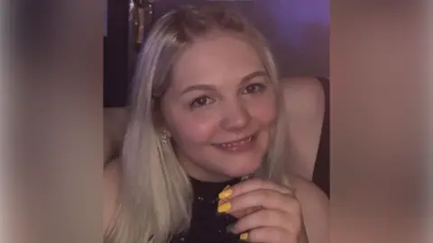 A head and shoulders shot of Libby Mycroft smiling at the camera. She has long, blonde hair and is wearing a black sparkly halterneck top.