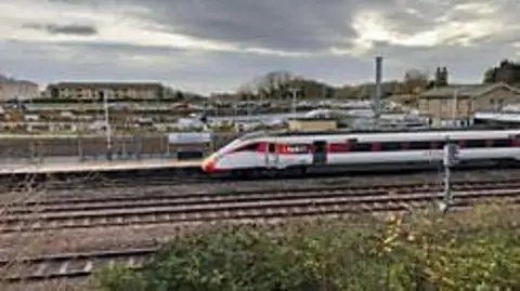 A passenger train at a platform, seen looking across the tracks.