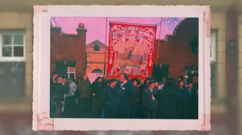 A group of miners gathered with a large red banner being held in the air.