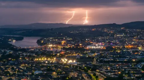 Shows bolts of lightning above a city at nighttime