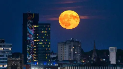 A glowing full moon against a Leicester skyline at night