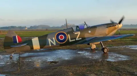 A kit-built replica Spitfire standing on a runway on a ckear day with its propeller turning