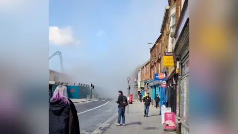 Onlookers look on in a city street as a large cloud of dust spreads into the air