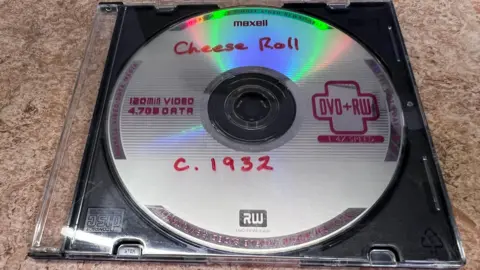 A DVD in a closed plastic case. It has "Cheese Roll c.1932" written on it in red marker pen. 