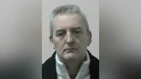 Northumbria Police Mugshot of Dellbridge. He is clean shaven and very pale faced, with short silver hair.