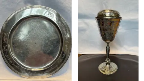 A silver plate on the left and a covered chalice on the right. Both of the items belong to a church.