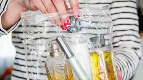 Woman's hand with red nail varnish places small bottles of toiletries in clear plastic bag