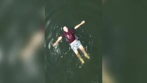 Man floating on his back in open water wearing a dark shirt