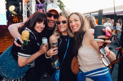 A group of people smile at the camera holding up drinks during an Alfresco Disco event in Bristol