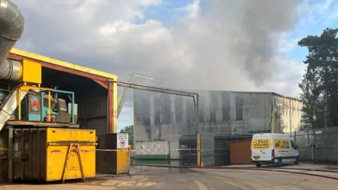 Clare Worden/BBC The outside of the PSH Environmental Ltd waste processing site on Wendover Road in Rackheath. There is smoke coming out of the site into the air. A white and yellow PSH Environmental Ltd van is parked outside the site.