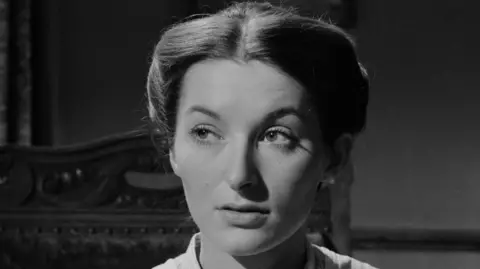 BBC The actress Vivien Heilbron in close-up black and white as Chris Guthrie, the main character in Sunset Song. Her hair is in a tight bun and she is sitting in a wooden chair looking to the left. She looks quizzical.