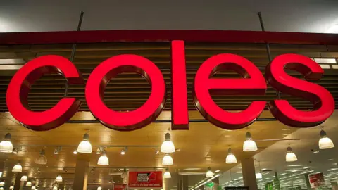 A large 'Coles' sign in front of supermarket lights