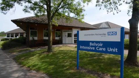The exterior of the Belvoir Intensive Care Unit which is a single storey brick building with a blue NHS sign outside the front.