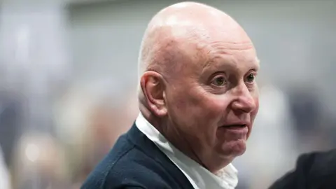 Getty Images Kevin Lee, a bald middle aged man in open neck shirt, looks on at the Makerfield by-election count