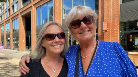 Nancy Hammond and Sian Couchman in Redhill. Nancy is wearing all black and Sian is wearing a blue top. Sian has her arm around Nancy, both women are wearing sunglasses.