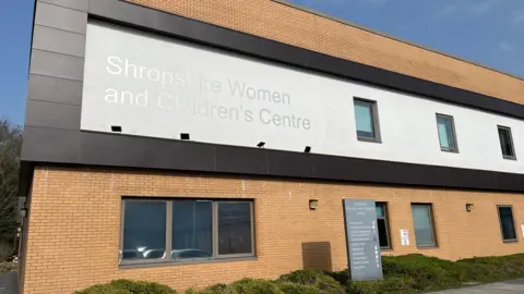 Ellen Knight/BBC The exterior of the Shropshire Women and Children's Centre at the Princess Royal Hospital in Telford. The building has two floors, and is built of light brown bricks. About seven grey-framed windows can be seen, and a large sign, in silver metal letters, reads 'Shropshire Women and Children's Centre' on the side of the building. Along the building's base is shrubbery, and the sky is blue and there is lots of sunshine. 