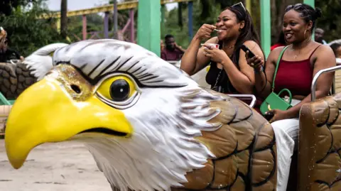 Amusement park visitors talk, smile and laugh as they ride a bird-shaped carousel at Magic Land on 29 June.