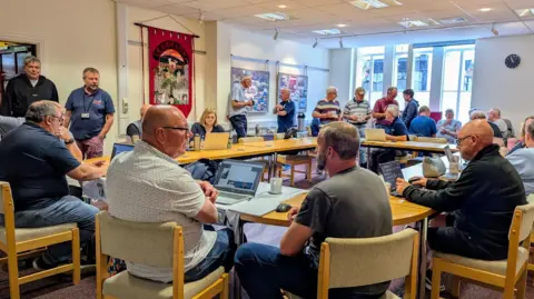 Veterans Regroup Project A large group of people sat around a table with laptops and paperwork, having a discussion.