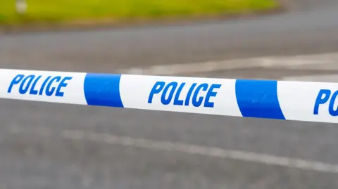 Generic image of police tape across a road. It is white with "POLICE" printed in blue.