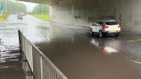 A silver car beside brown water on the road in the underpass at Blacks Road in Belfast.