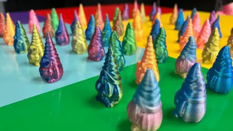 A table full of tiny gnome figures in an array of different colours. The gnomes have tall pointed hats and large beards.
