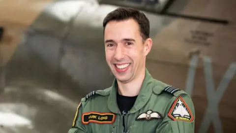 RAF Sqn Ldr Mark Long standing in front of a Spitfire