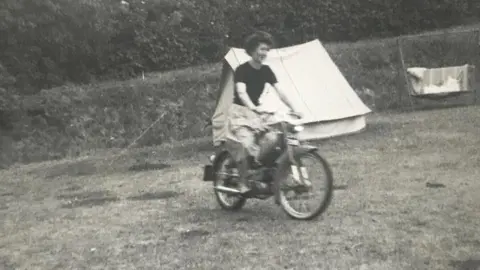 Fiona Dryden Dorothy Graham in a black and white picture ridig a motorbike with a tent behind