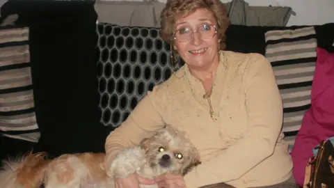 Family photograph Pat sitting on a settee holding a dog and smiling