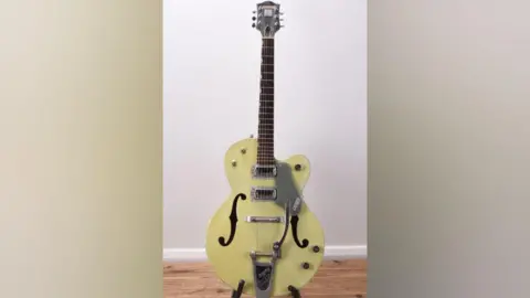 Halls Fine Art Auctioneers A light green guitar on a stand. It has a Gretsch logo on it.