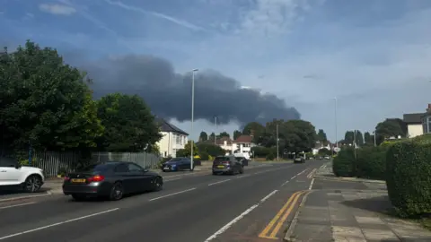 A large plume of smoke can be seen from a pavement at the side of a road in Liverpool.