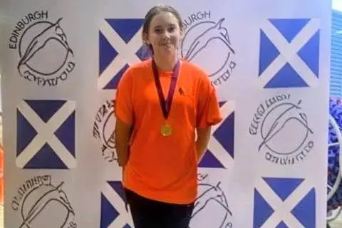 Heather Graham A young teenage girl wearing an orange t-shirt with a gold medal around her neck stands on a podium.