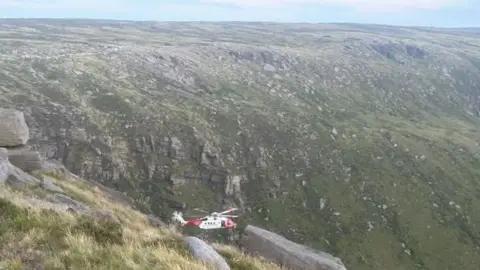 A helicopter flies into a steep rocky valley 
