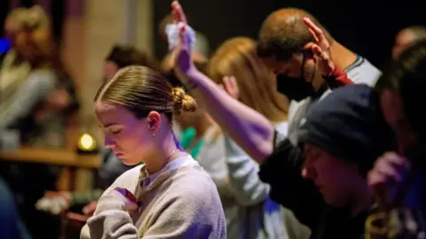 A young women has closed eyes and a bowed head at a worship services